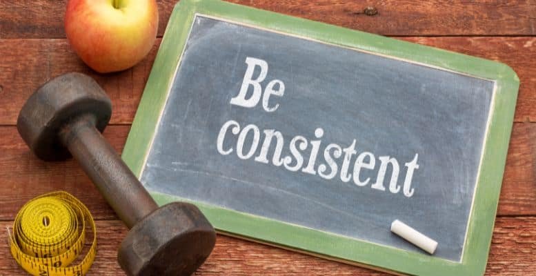 Chalk board with Be consistant written next to an apple and dumbell